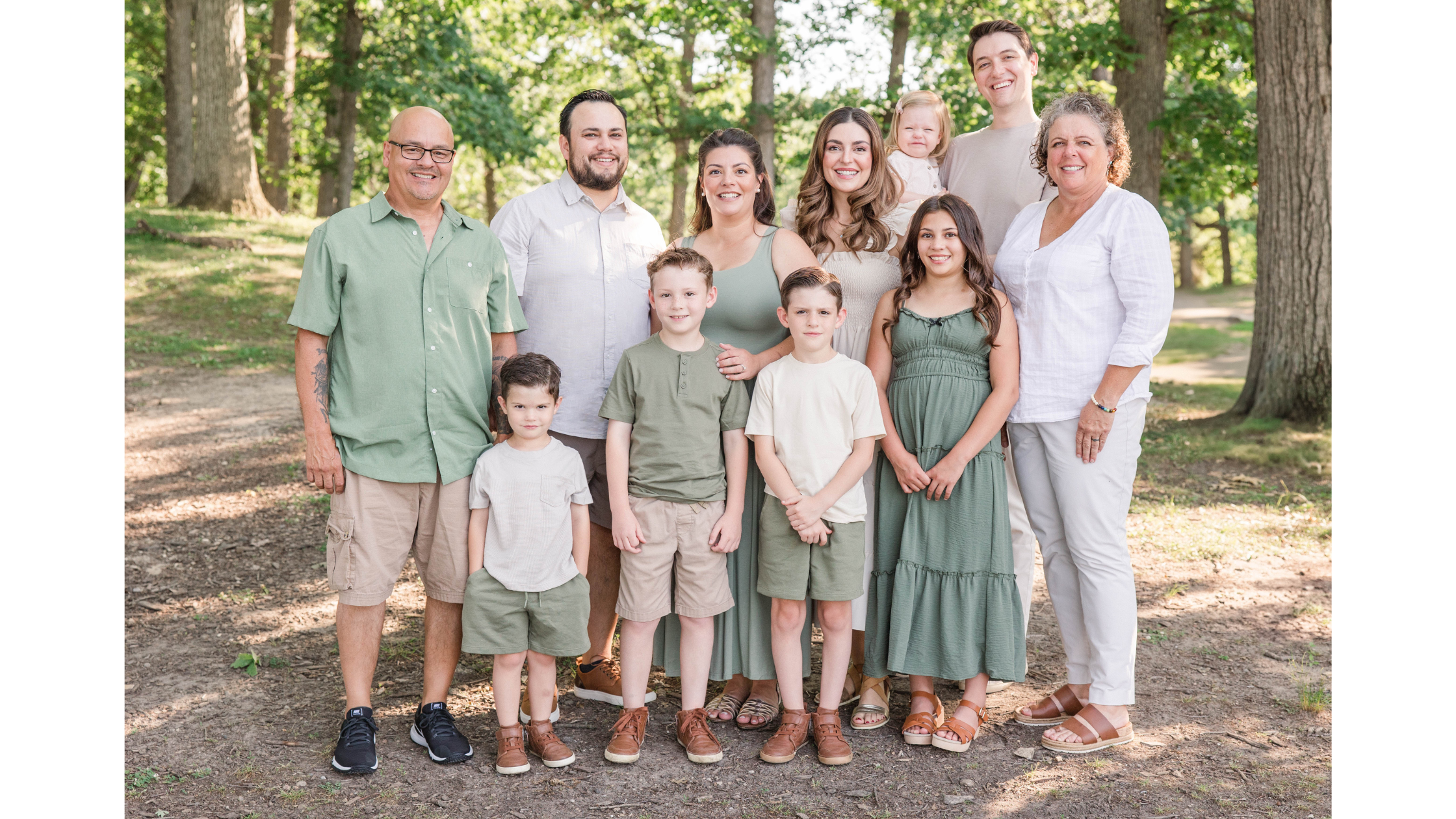 Extended family smiling at camera during golden hour in a woodsy park in Howell, Michigan. Multi-generational photo in natural light.